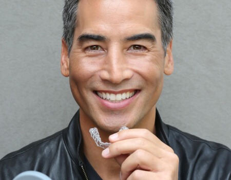 Man with dark, gray-streaked hair holding a Spark Aligner, available in Bee Cave from Dr. Alberto Tostado