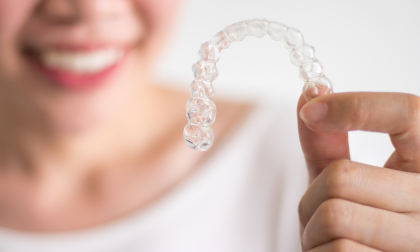 Close-up hands of a woman holding clear aligners, such as Essix retainers