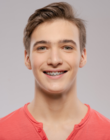 Teenage boy wearing coral shirt smiling with braces, for information on affordable braces in Bee Cave.
