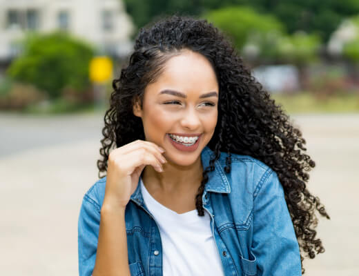 Young woman with long, wavy dark hair and braces smiling, from Lake Travis Orthodontics in Bee Cave.