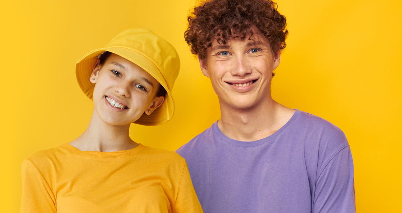 Two young people smiling against a yellow background